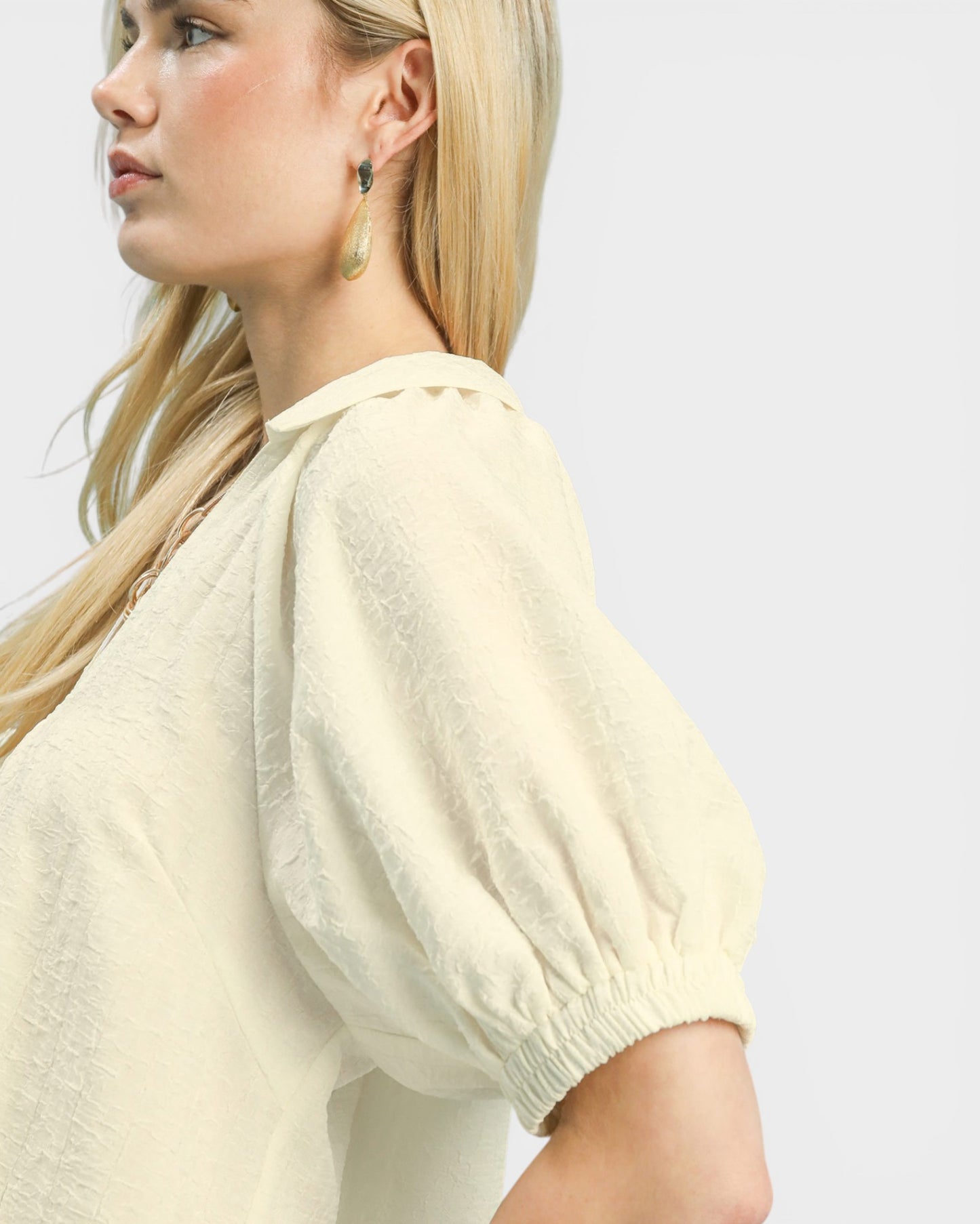 Woman wearing a light-colored blouse with puffed sleeves on a plain background