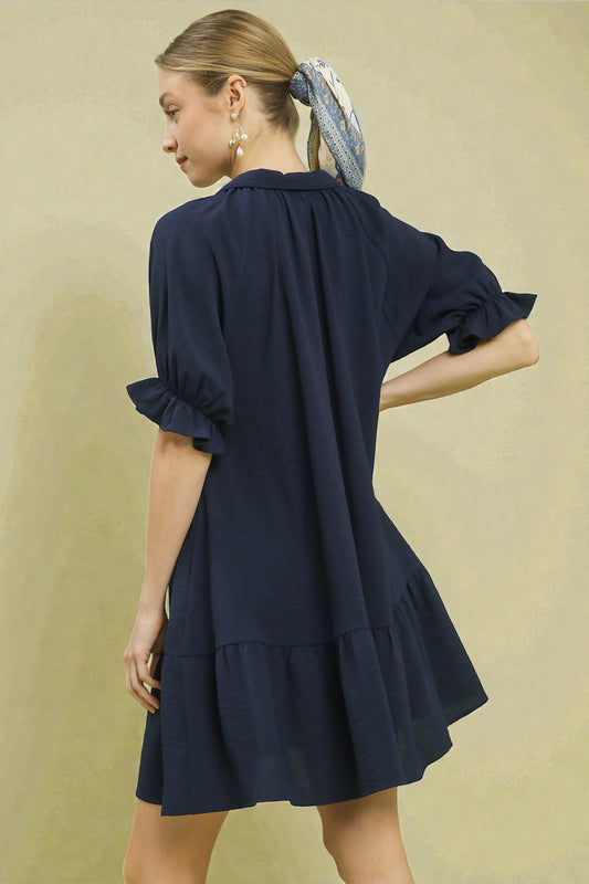 Woman wearing a navy blue dress with puff sleeves against a beige background