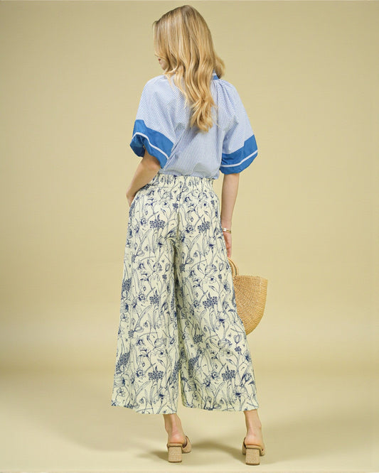 Woman wearing a light blue top with blue sleeves and floral pants on a beige background