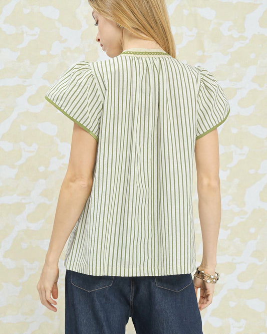 Woman wearing a green and white striped shirt with short sleeves against a beige patterned background