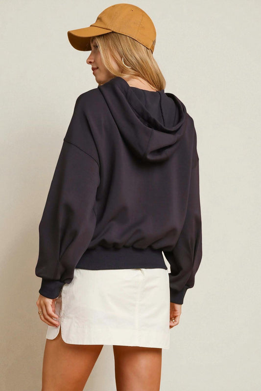 Person wearing a black hoodie, white shorts, and a tan cap on a beige background