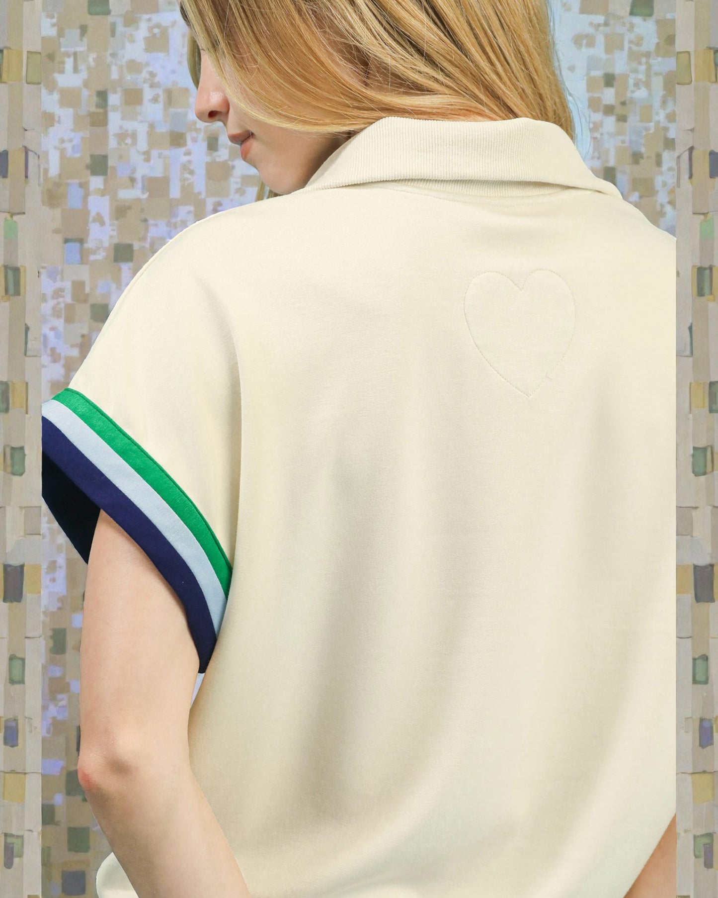 Person wearing a cream-colored shirt with a colorful striped sleeve against a mosaic tile wall.