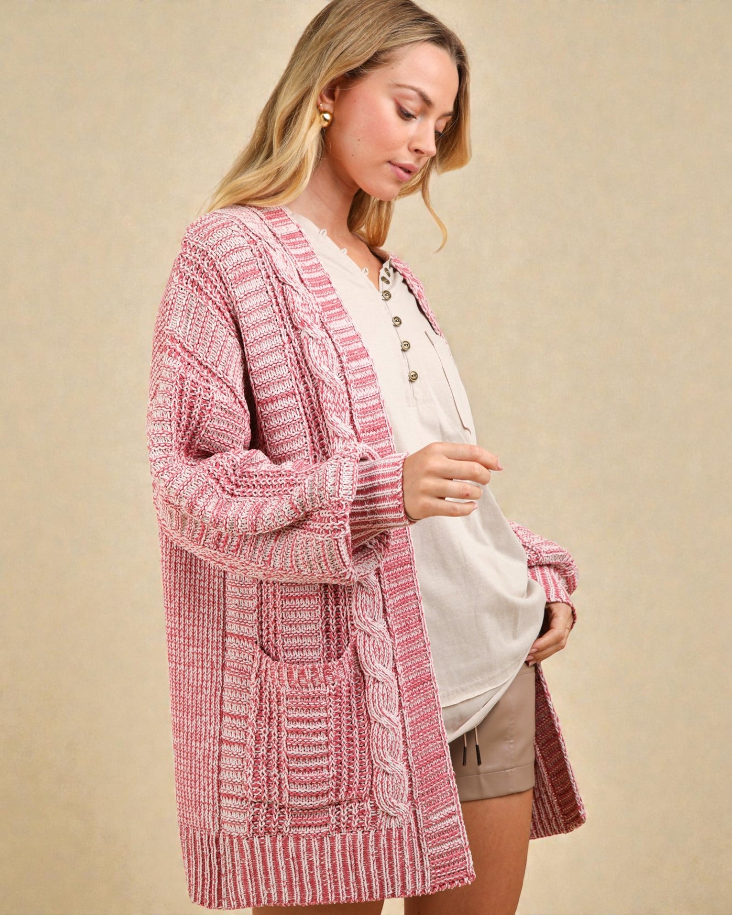 Woman wearing a pink and white striped cardigan over a white shirt and shorts on a beige background