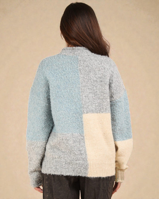 Person wearing a color-blocked sweater with blue, gray, and beige sections on a beige background