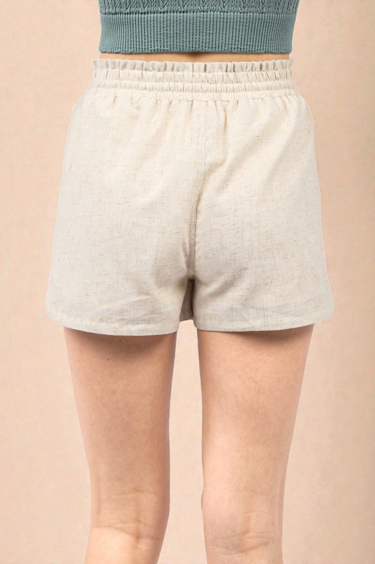 Person wearing light gray shorts on a beige background