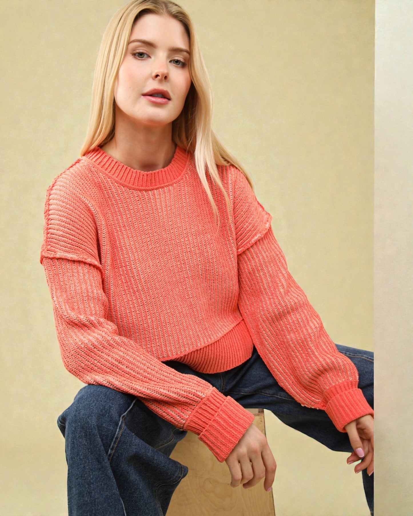Woman wearing a coral sweater sitting on a beige surface