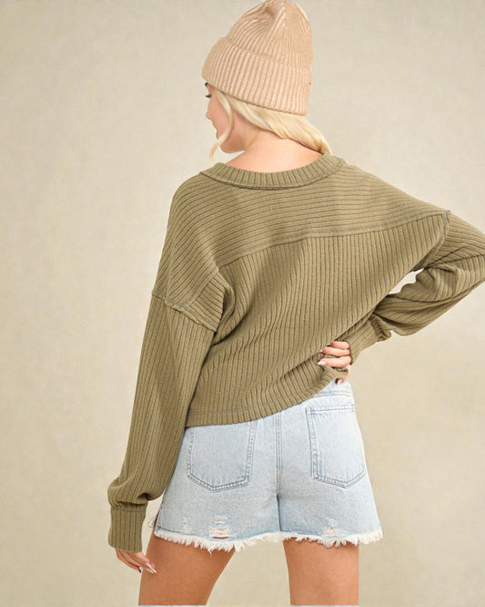 Person wearing a green sweater and light blue shorts with a beige beanie on a plain background