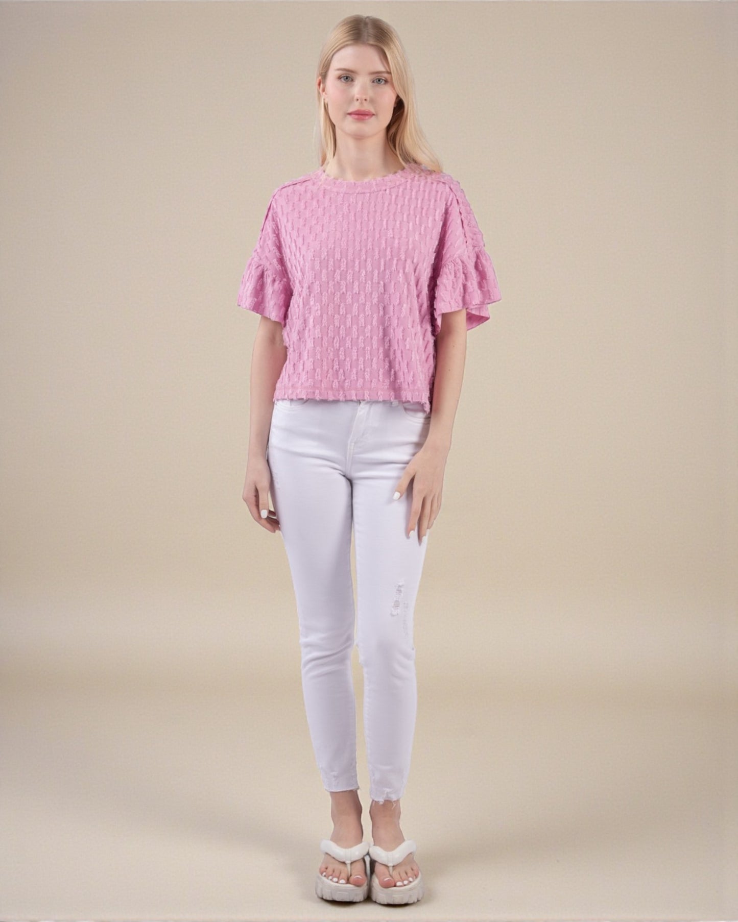 Woman wearing a pink textured top and white pants on a beige background
