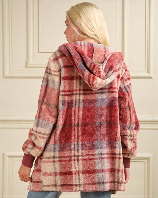 Person wearing a red and beige plaid hoodie with a hood, standing against a white wall.