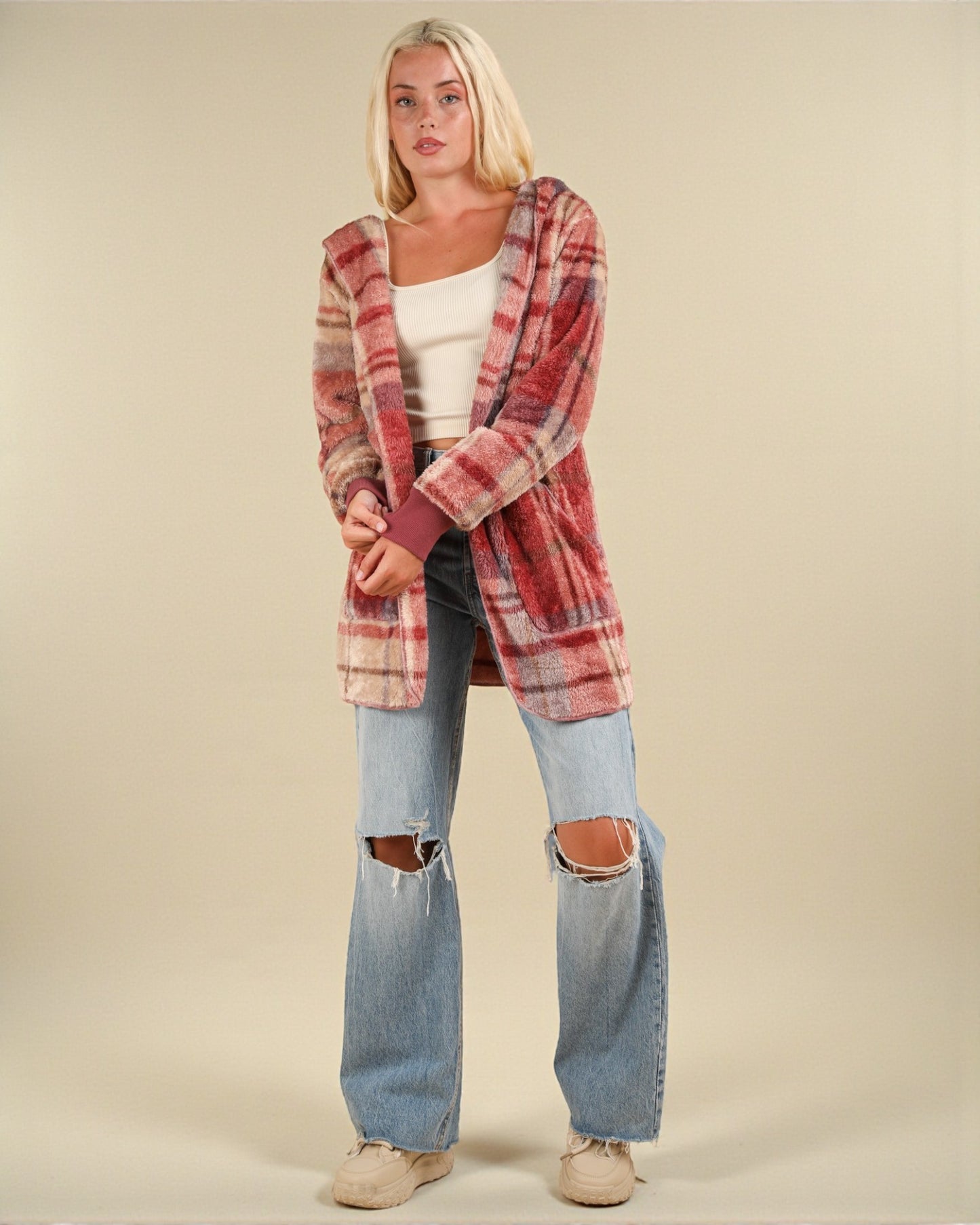 Woman wearing a plaid shirt and ripped jeans on a beige background