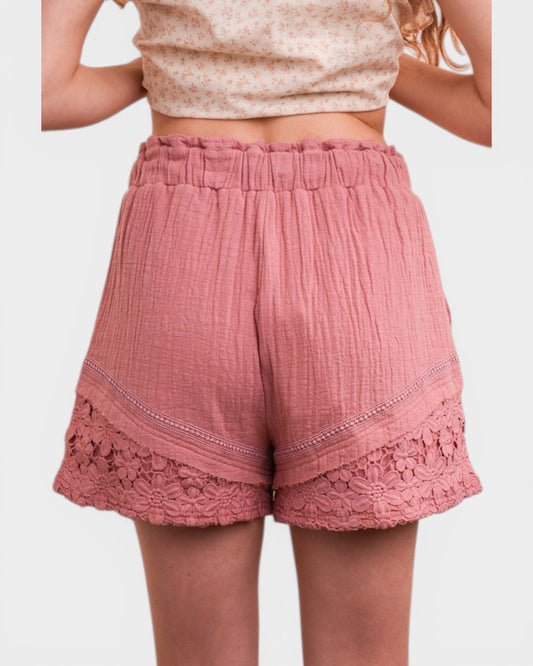 Pink shorts with lace trim worn by a person on a white background
