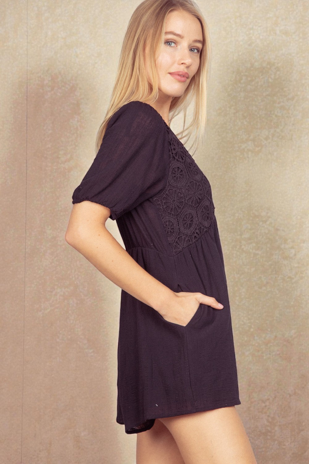 Woman wearing a black romper with lace details on a beige background