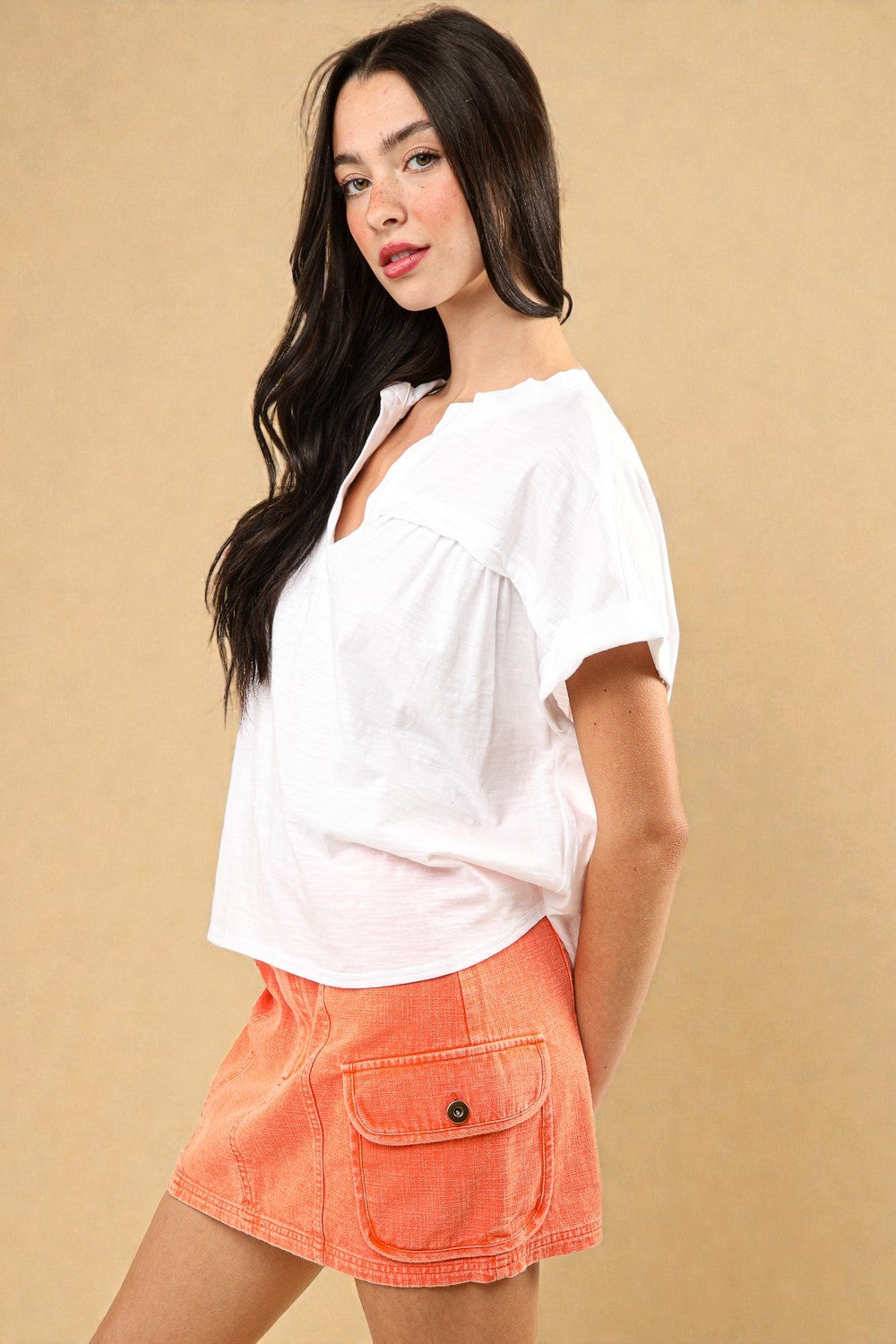 Woman wearing a white top and orange shorts against a beige background