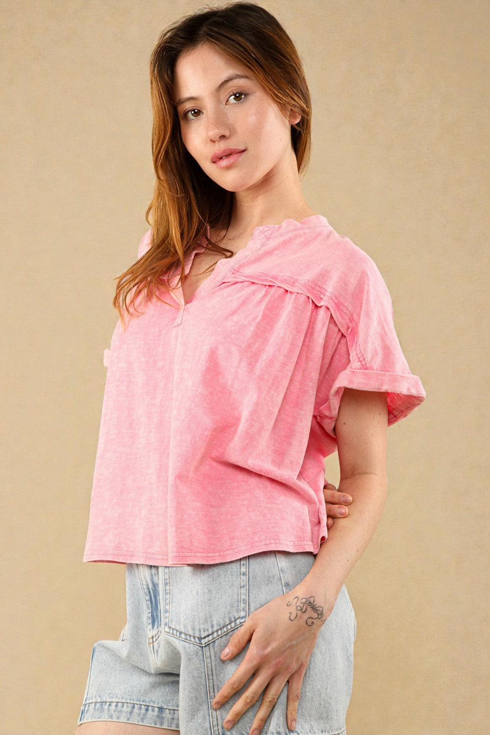 Woman wearing a pink top and denim shorts against a beige background