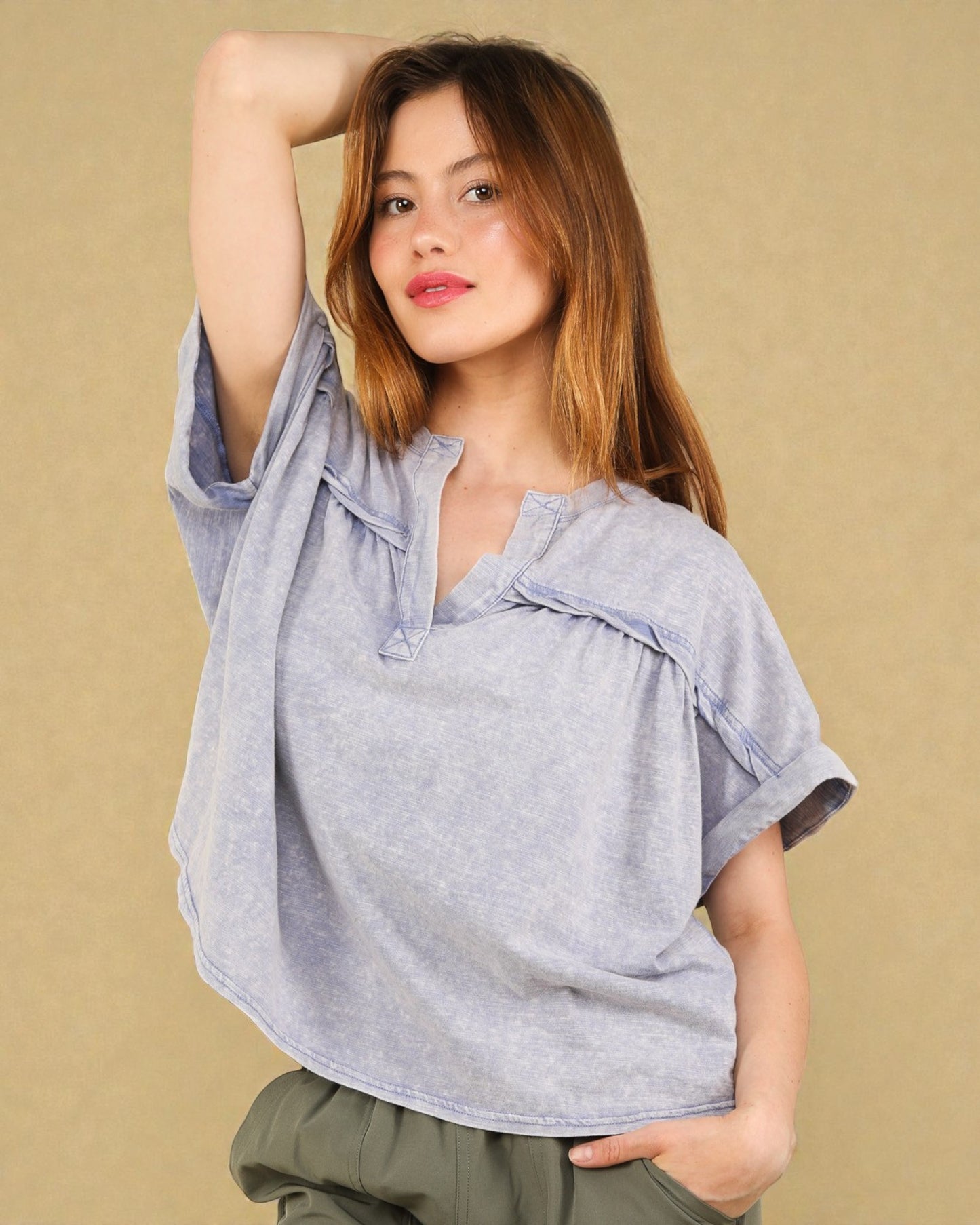 Woman wearing a light blue blouse with ruffled details against a beige background