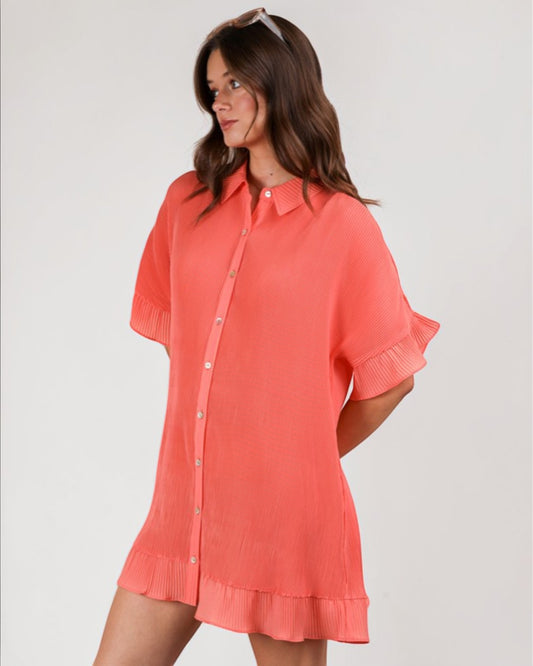 Woman wearing a coral shirt dress against a plain background