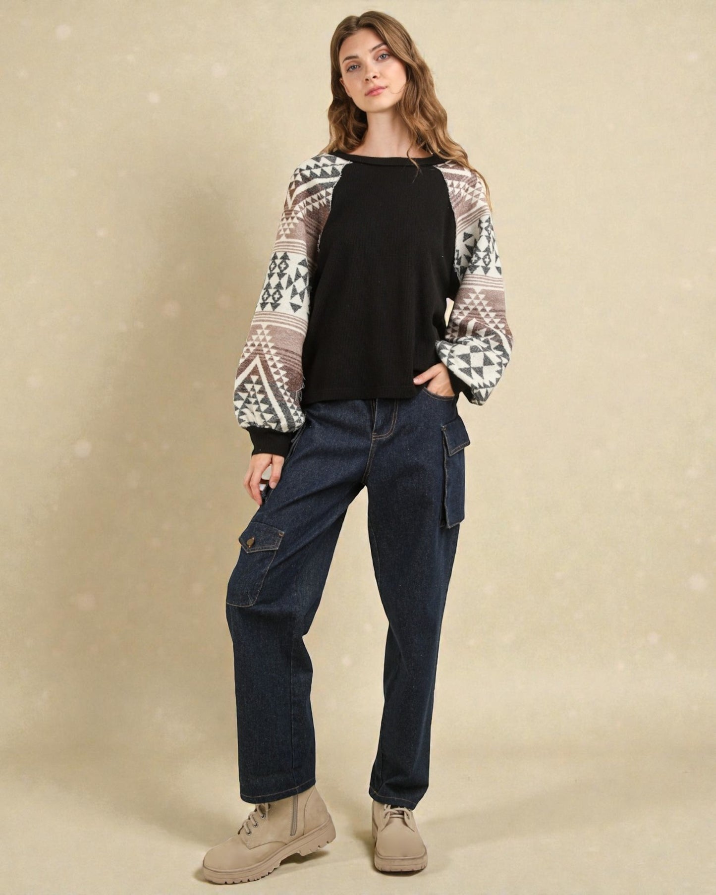 Woman wearing a patterned cardigan, black top, and blue jeans on a beige background