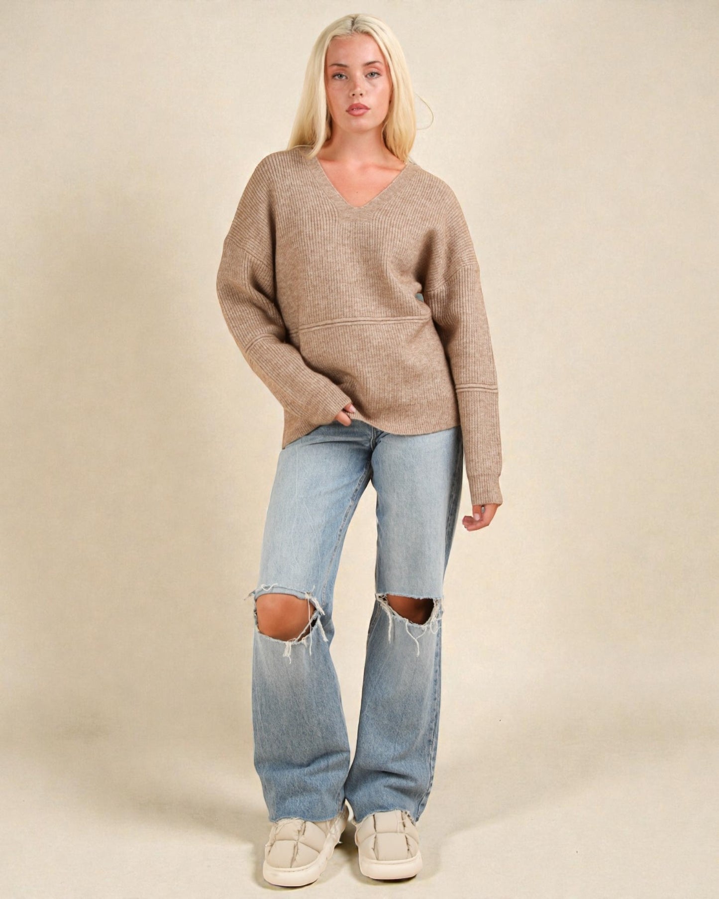 Woman wearing a brown sweater and ripped jeans on a beige background