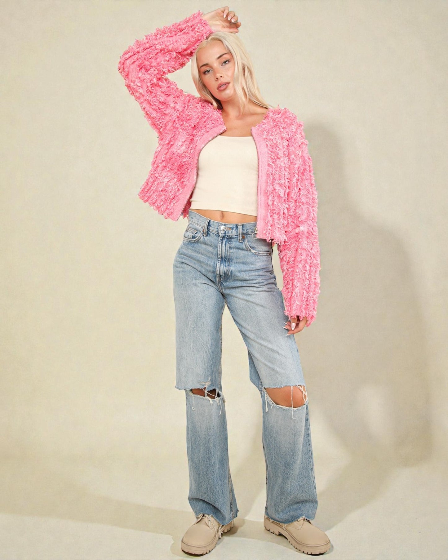 Person wearing a pink fuzzy jacket, white top, and ripped jeans on a neutral background