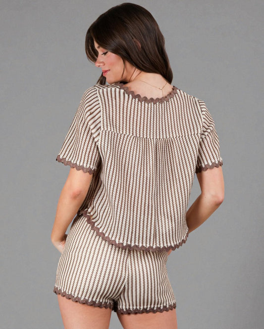 Woman wearing a matching top and shorts set with ruffled details on a gray background