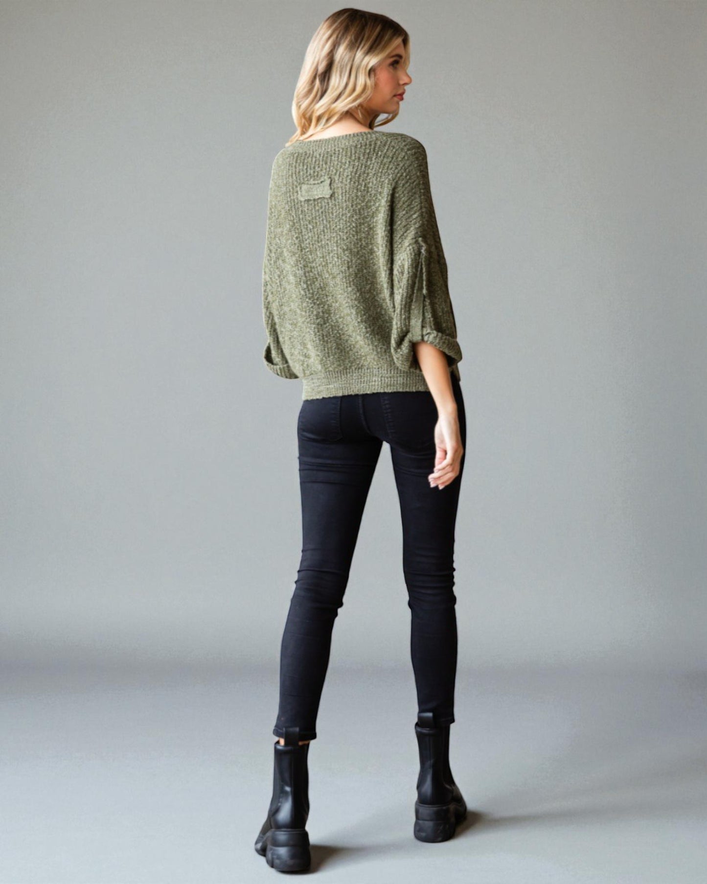 Person wearing a green sweater and black pants on a plain background