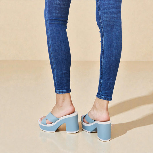 Person wearing blue platform sandals and jeans on a beige background