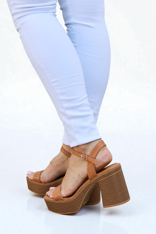 Brown platform sandals worn with white pants on a white background