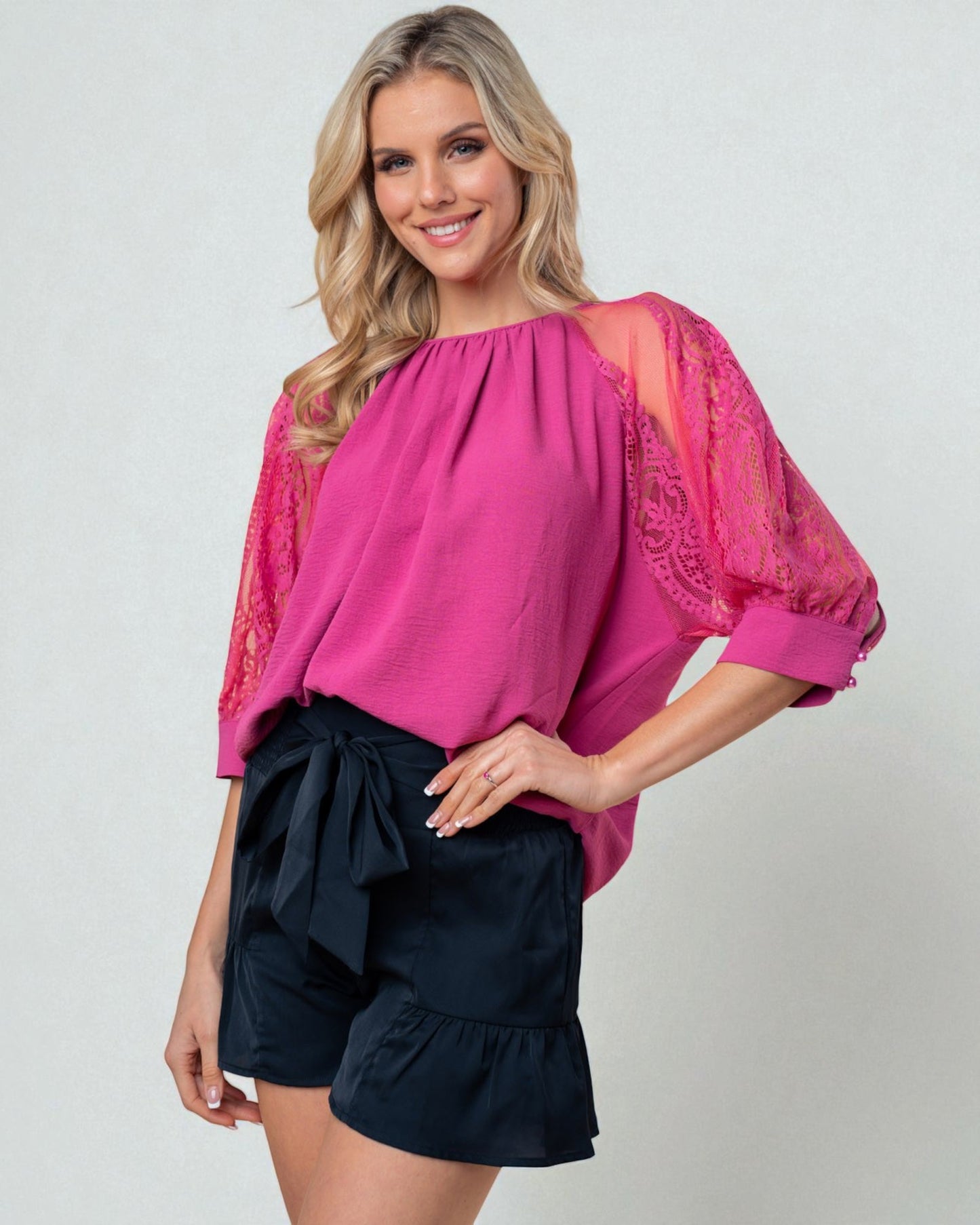 Woman wearing a pink blouse with lace sleeves and black shorts on a white background