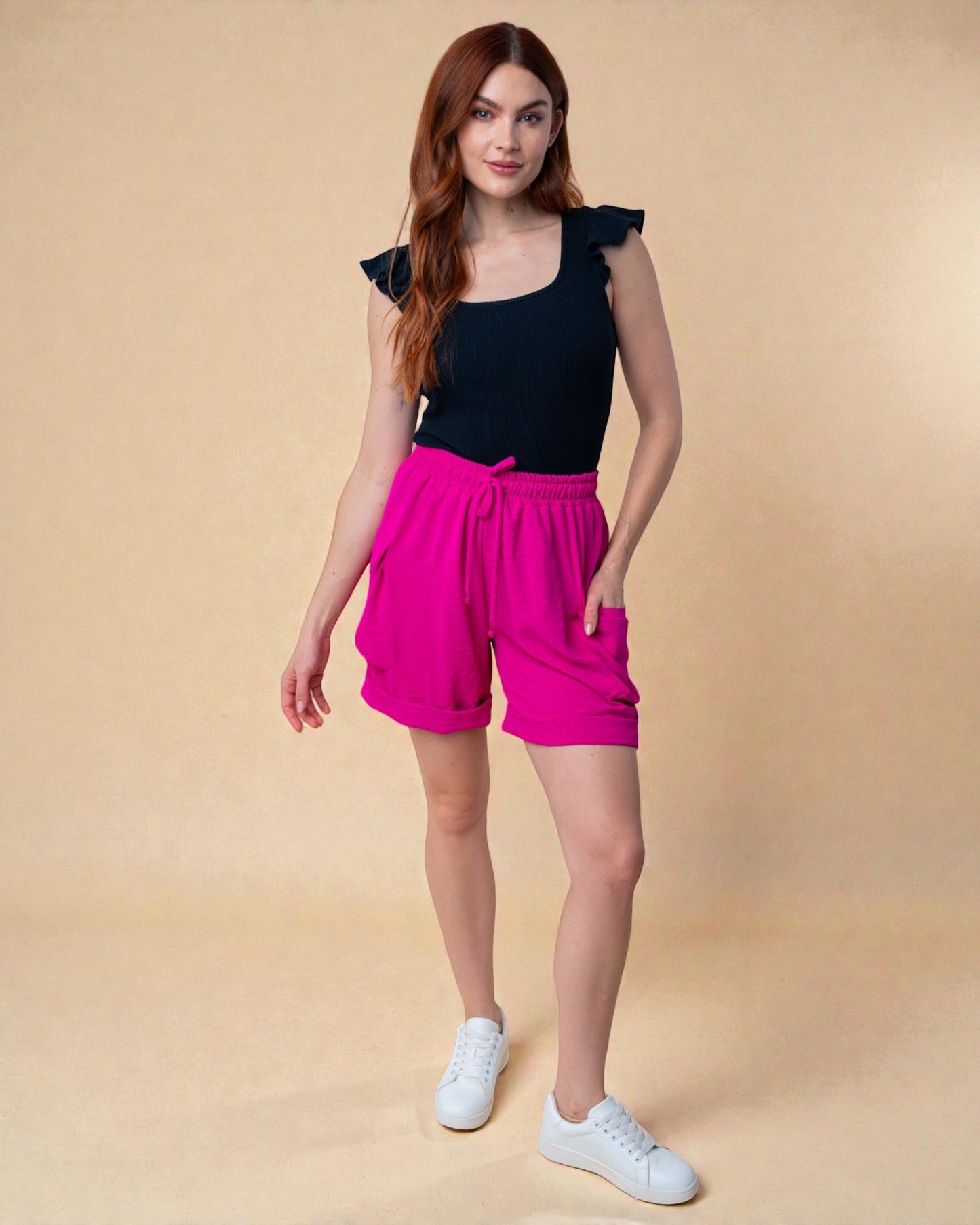 Woman wearing a black top and pink shorts on a beige background