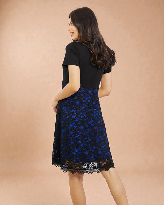 Woman wearing a black top and blue lace skirt on a beige background