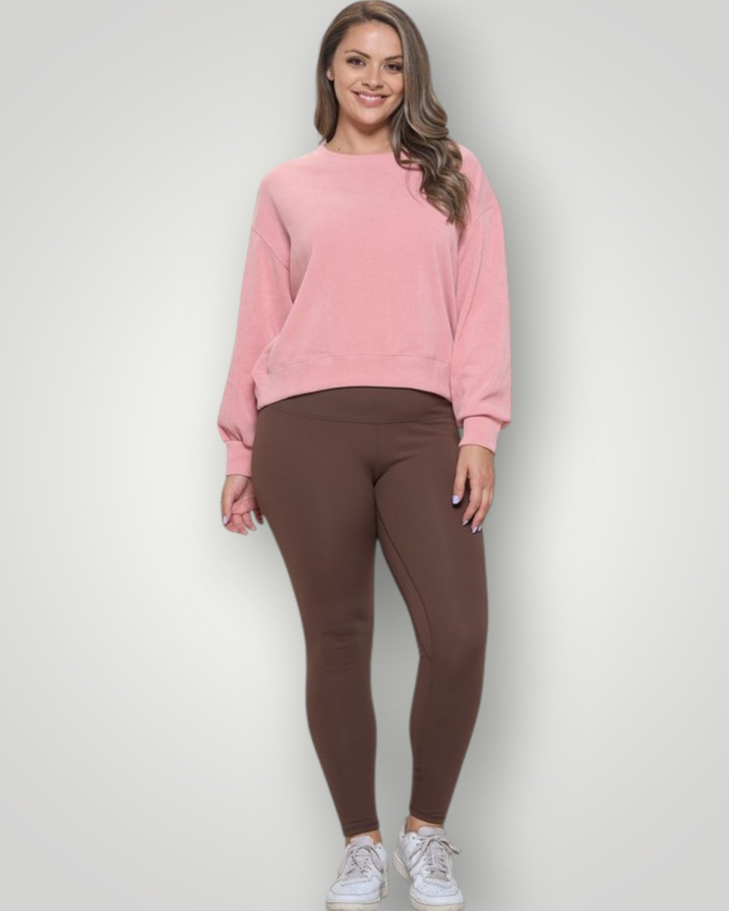 Woman wearing a pink sweatshirt and brown leggings on a white background
