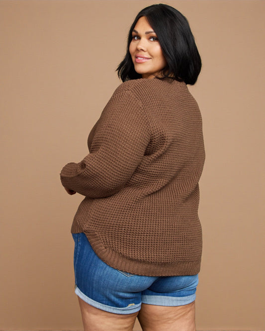 Woman wearing a brown sweater and blue shorts on a beige background
