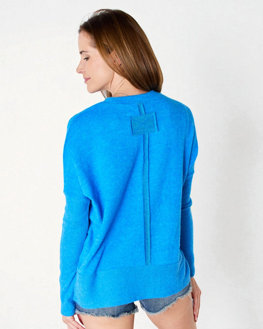 Woman wearing a blue sweater with a unique back design on a white background