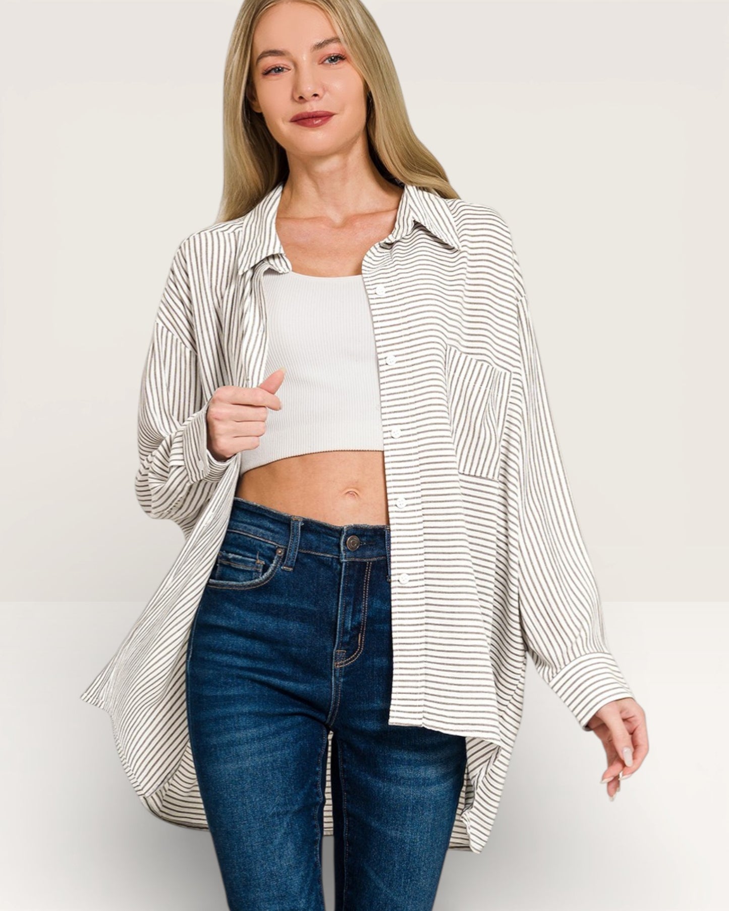 Woman wearing a striped shirt over a white top and blue jeans on a plain background