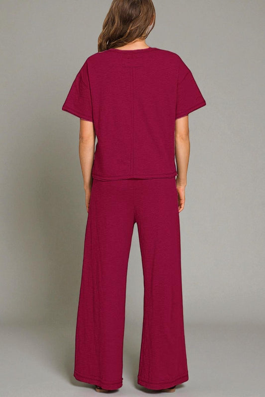 Person wearing a maroon outfit with wide-leg pants on a plain background
