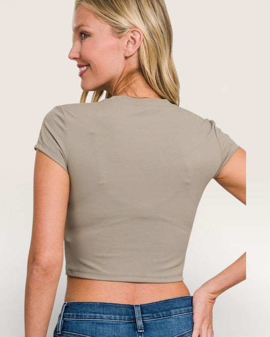 Woman wearing a beige crop top and blue jeans against a plain background