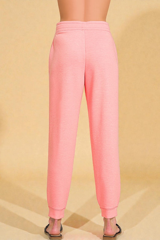 Pink sweatpants worn by a person on a beige background
