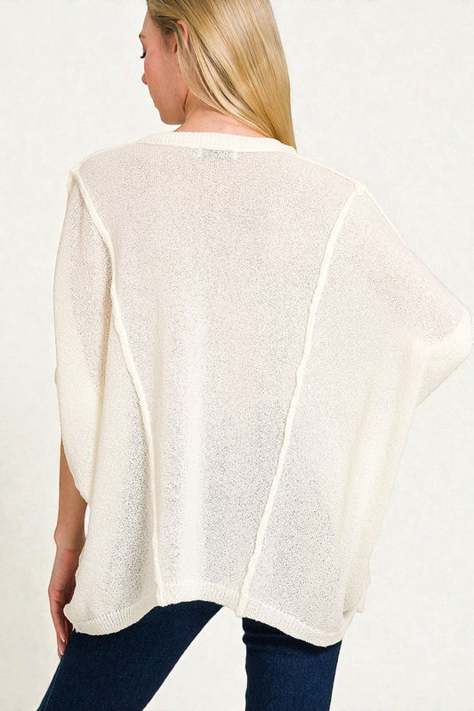 Woman wearing a white poncho over a blue outfit on a plain background