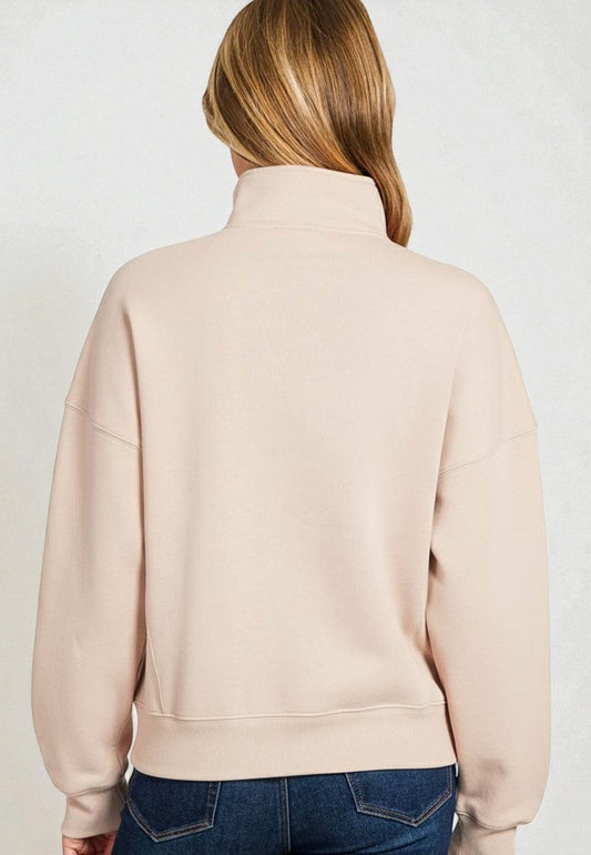 Person wearing a beige sweatshirt and blue jeans on a plain background