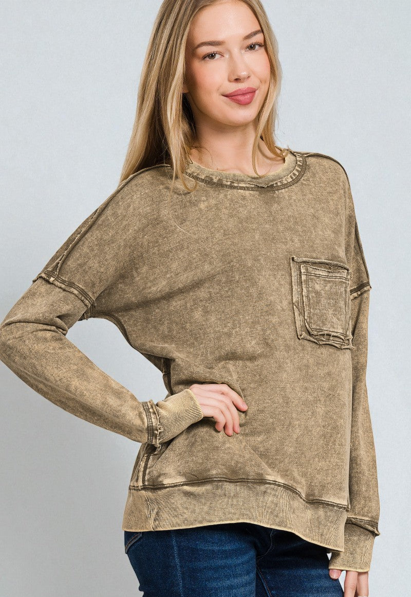Woman wearing a brown long-sleeve top with a pocket on a gray background