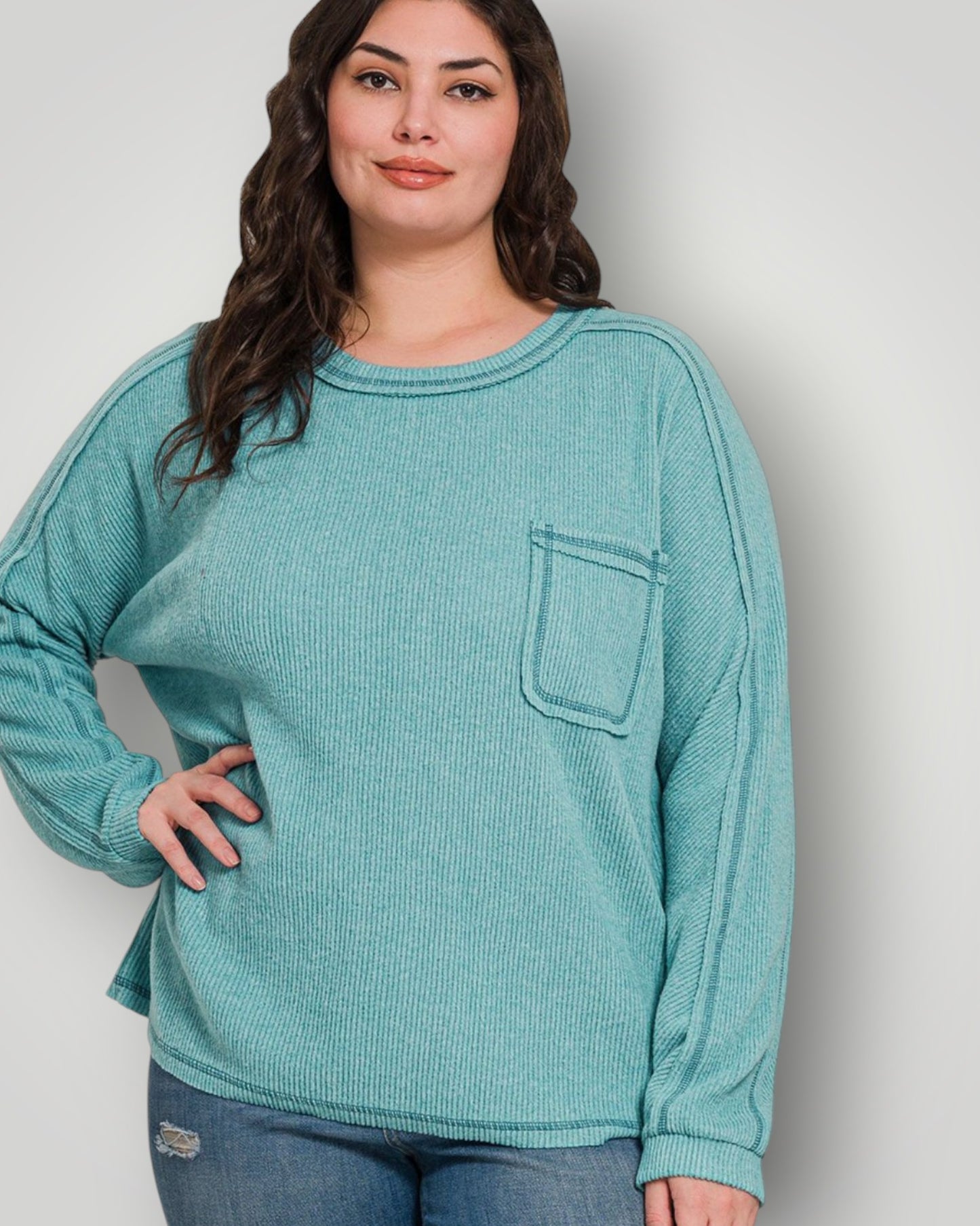 Woman wearing a teal long-sleeve shirt with a pocket on a plain background