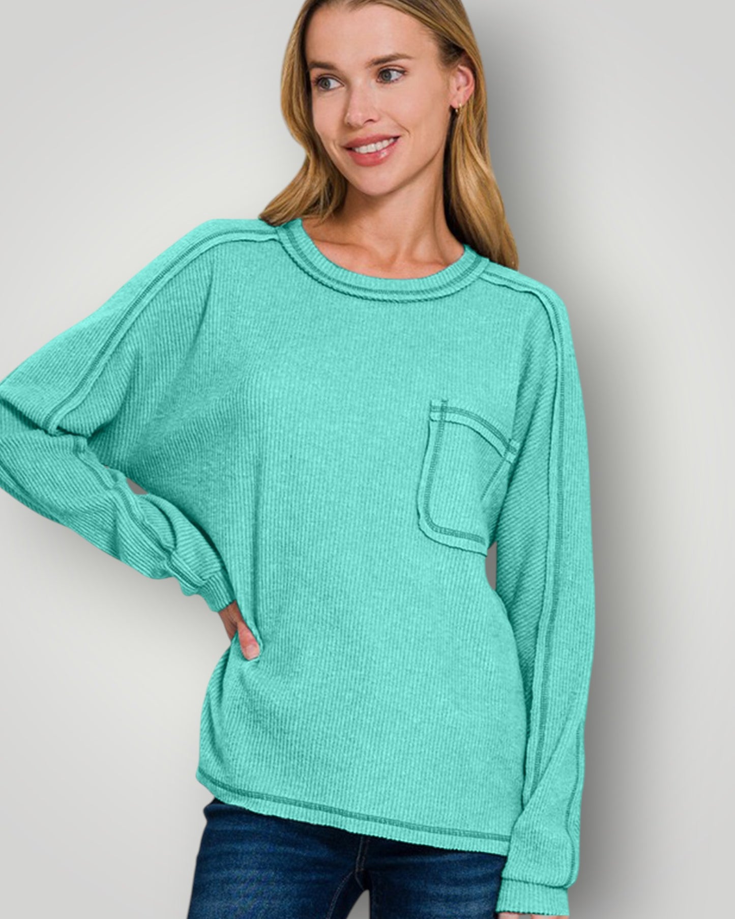 Woman wearing a teal sweater with a pocket on a plain background
