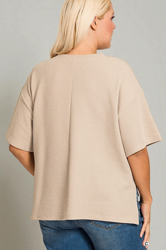 Person wearing a beige ribbed sweater and blue jeans on a gray background