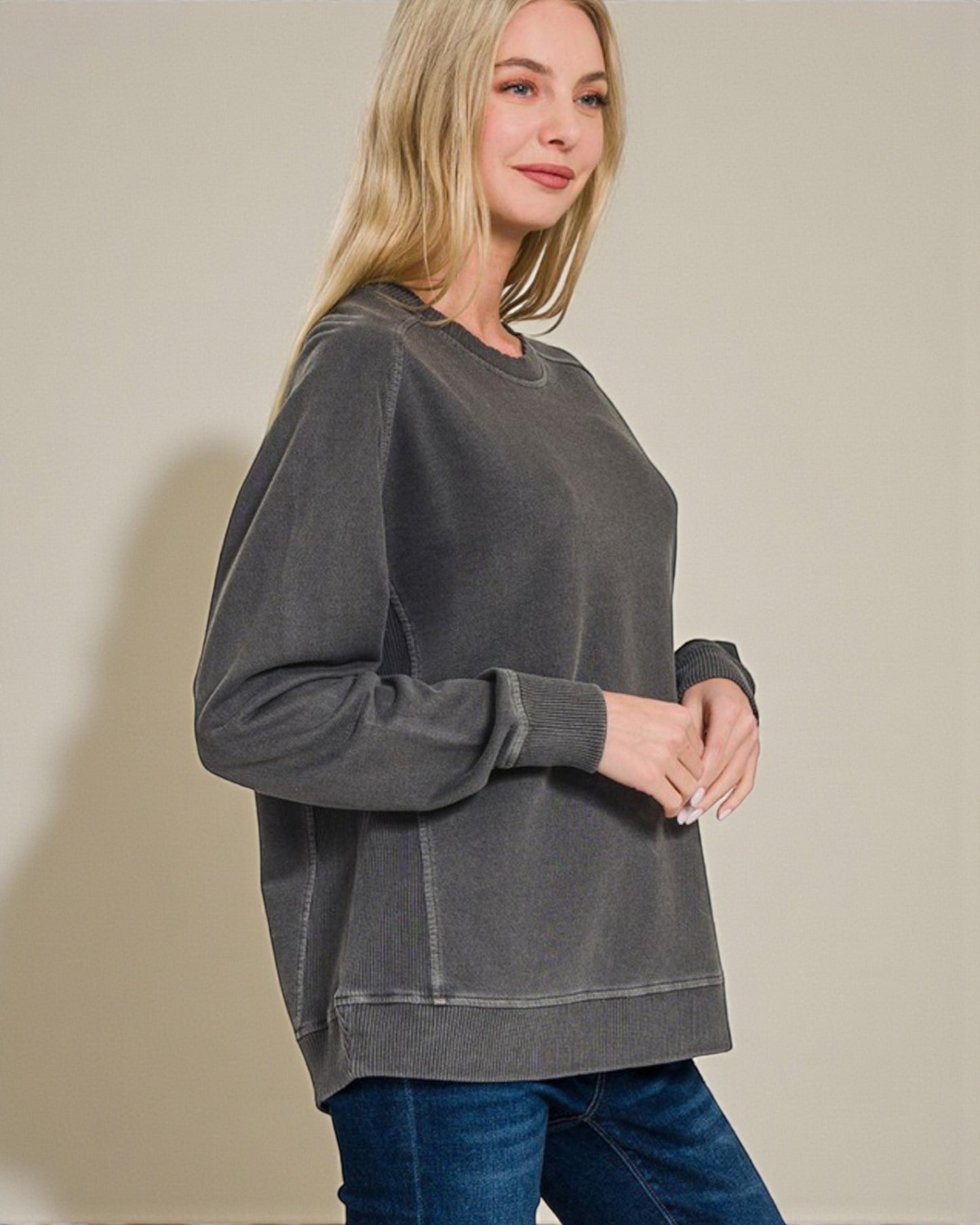Woman wearing a gray sweatshirt and blue jeans against a beige background
