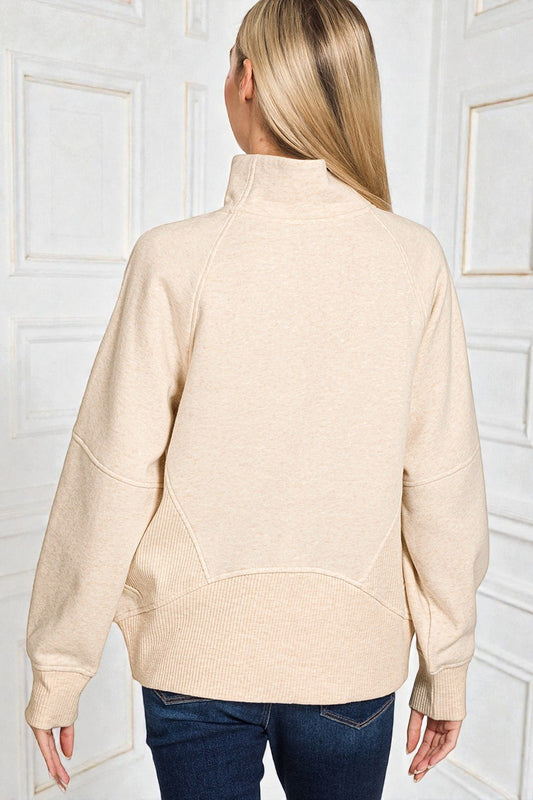 Woman wearing a beige sweater against a white paneled wall