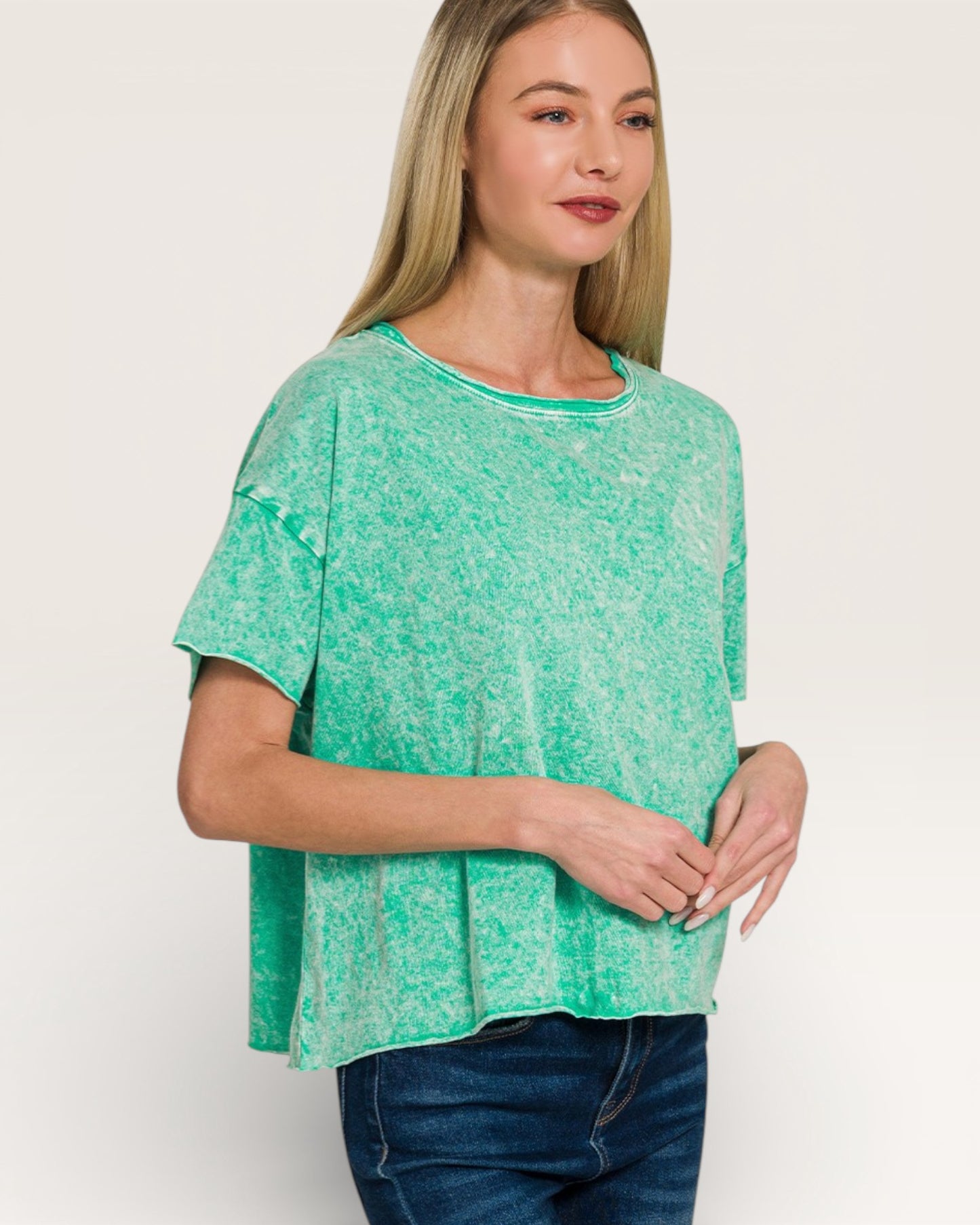 Woman wearing a green patterned top and blue jeans on a white background