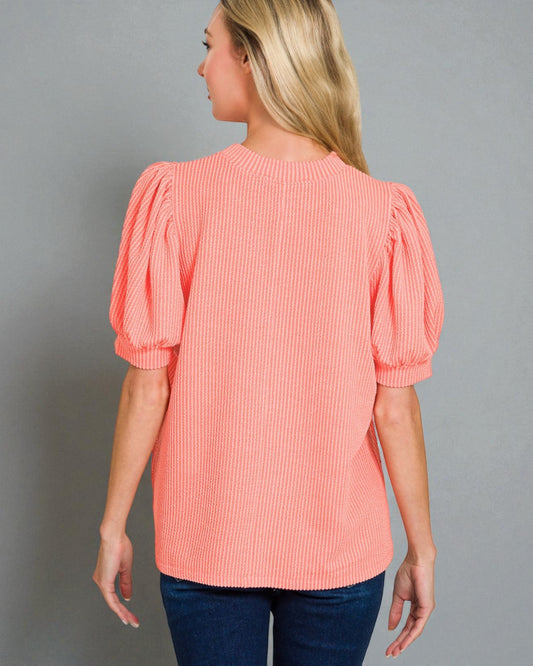 Woman wearing a coral blouse with puff sleeves against a gray background