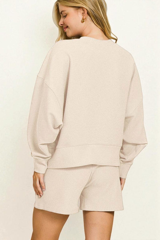 Woman wearing a beige sweatshirt and shorts set on a plain background