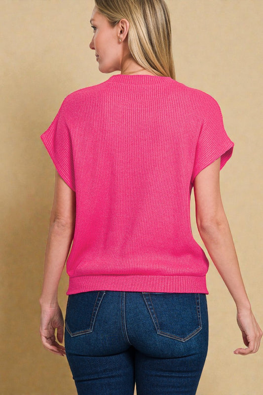 Woman wearing a bright pink sweater and blue jeans on a beige background