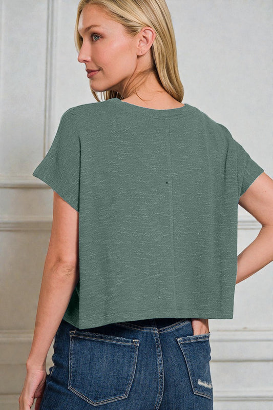 Woman wearing a green t-shirt and blue jeans against a neutral background